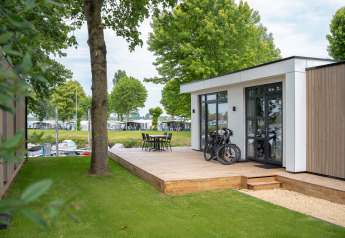 Lodge moderno con terraza de madera, bicicletas y muebles exteriores en Villa Maritiem, MarinaPark Bad Nederrijn, Países Bajos.