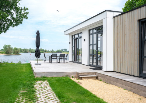 Lodge moderno sul lago con terrazza in legno, tavolo da pranzo e vista sull’acqua nei Paesi Bassi.