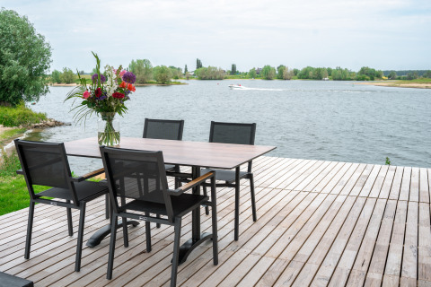 Conjunto de comedor al aire libre en una terraza de madera con vistas al lago en Villa Maritiem, MarinaPark Bad Nederrijn.