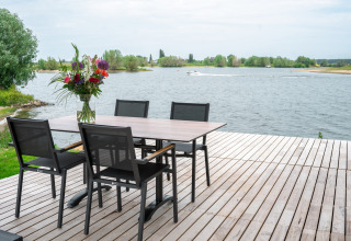 Conjunto de comedor al aire libre en una terraza de madera con vistas al lago en Villa Maritiem, MarinaPark Bad Nederrijn.