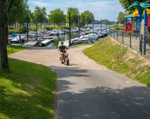 Persona en scooter junto a MarinaPark Bad Nederrijn, con barcos y parque infantil en Villa Maritiem.