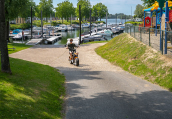Person riding a scooter at MarinaPark Bad Nederrijn with boats and playground by Villa Maritiem, Netherlands.