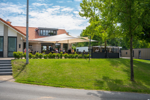 Udendørs siddeområde ved Villa Maritiem lodge på MarinaPark Bad Nederrijn i Holland, solrigt med grønne omgivelser.