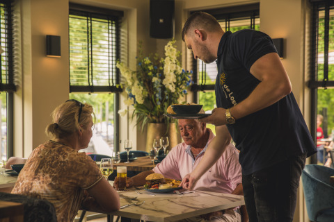 Un camarero sirve comida a dos comensales en una mesa acogedora del restaurante Villa Maritiem.