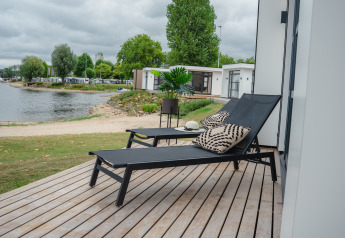 Terrasse ensoleillée avec transats et coussins à la Villa Maritiem, vue sur le lac à MarinaPark Bad Nederrijn, Pays-Bas.
