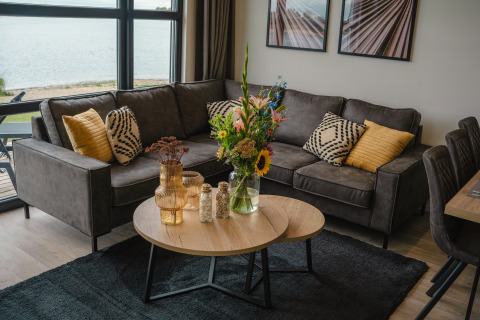 Soggiorno a Villa Maritiem al MarinaPark Bad Nederrijn, Paesi Bassi, con divano grigio, cuscini e fiori.
