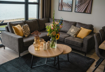Sala de estar en Villa Maritiem en MarinaPark Bad Nederrijn, Países Bajos, con sofá gris, cojines y flores.