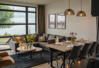 Salón y comedor modernos con vista al lago en Villa Maritiem, MarinaPark Bad Nederrijn, Países Bajos.