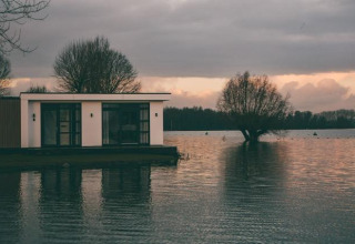 Villa moderna junto al agua en MarinaPark Bad Nederrijn, Países Bajos, al atardecer, rodeada de árboles.