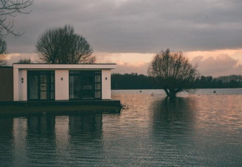 Villa moderna junto al agua en MarinaPark Bad Nederrijn, Países Bajos, al atardecer, rodeada de árboles.