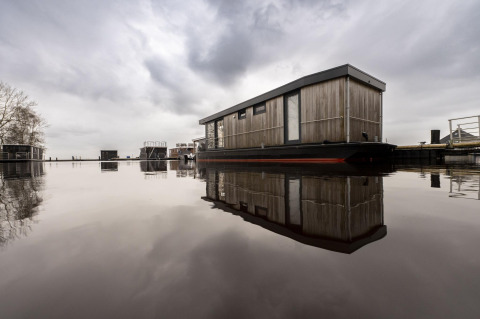Houseboat moderna chiamata Offingawier a Welcome In - Friesland, Paesi Bassi, riflessa sull'acqua calma.