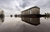 Casa flotante moderna llamada Houseboat Offingawier en Welcome In - Friesland, Países Bajos, reflejada en el agua.