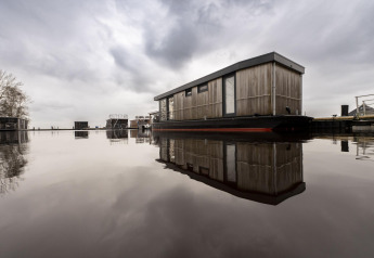 Houseboat moderna chiamata Offingawier a Welcome In - Friesland, Paesi Bassi, riflessa sull'acqua calma.