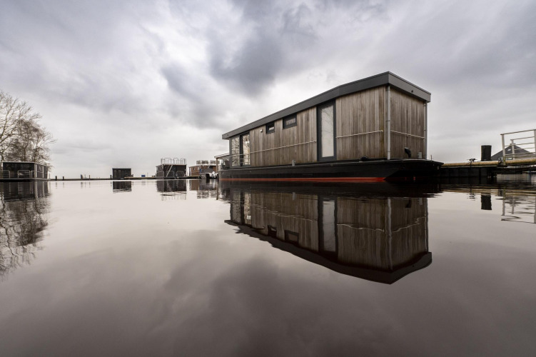 Casa flotante moderna llamada Houseboat Offingawier en Welcome In - Friesland, Países Bajos, reflejada en el agua.
