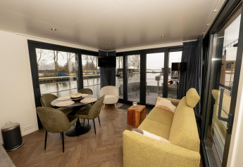 Salon du houseboat Offingawier à Friesland, Pays-Bas, vue sur l’eau et grande baie vitrée, déco moderne.