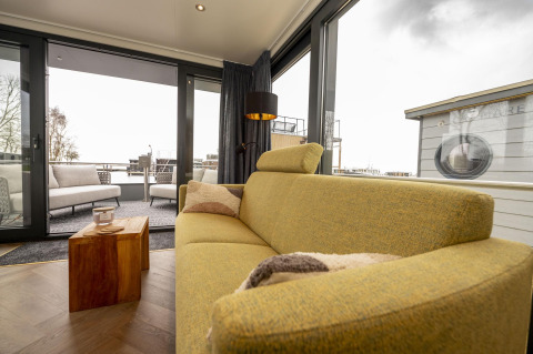 Sala de estar con sofá moderno en Houseboat Offingawier en Welcome In - Friesland, Países Bajos, vista al exterior.