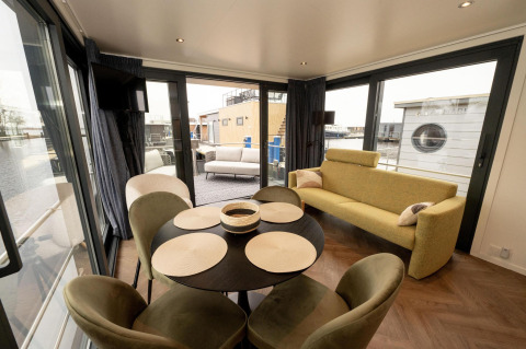 Espacio luminoso y moderno en un botecasa con mesa de comedor, sofá y amplias ventanas al agua en Frisia, Países Bajos.