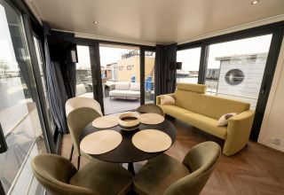 Espacio luminoso y moderno en un botecasa con mesa de comedor, sofá y amplias ventanas al agua en Frisia, Países Bajos.