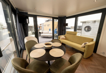 Espacio luminoso y moderno en un botecasa con mesa de comedor, sofá y amplias ventanas al agua en Frisia, Países Bajos.
