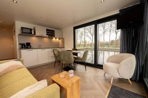 Sala de estar con cocina moderna y mesa de comedor en una casa flotante con vistas al agua en Offingawier, Friesland.