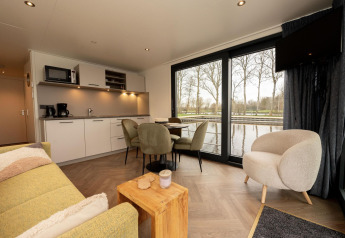 Sala de estar con cocina moderna y mesa de comedor en una casa flotante con vistas al agua en Offingawier, Friesland.