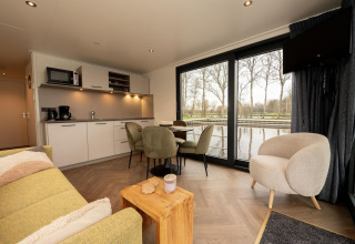 Stue med moderne køkken og spisebord på en husbåd med udsigt over vandet i Offingawier, Friesland.