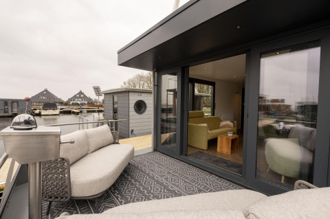 Zona lounge esterna su Houseboat Offingawier con divani moderni e vista sull’acqua in Frisia, Paesi Bassi.