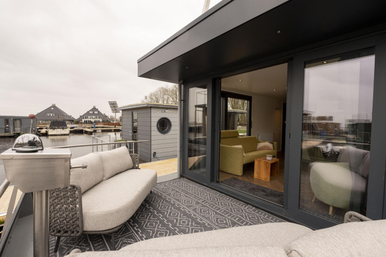 Zona de estar exterior en Houseboat Offingawier con vistas al agua y cómodos asientos en Friesland, Países Bajos.