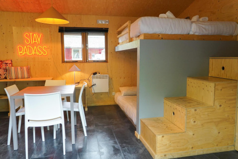 Cabaña Forest Lodge en Het Amsterdamse Bos, literas, mesa de comedor y letrero neón Stay Badass.