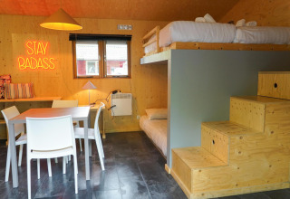 Cabaña Forest Lodge en Het Amsterdamse Bos, literas, mesa de comedor y letrero neón Stay Badass.