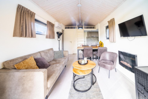 Gezellige woonkamer in de Tiny House bij De Wije Werelt in Nederland met bank, tafel en televisie.