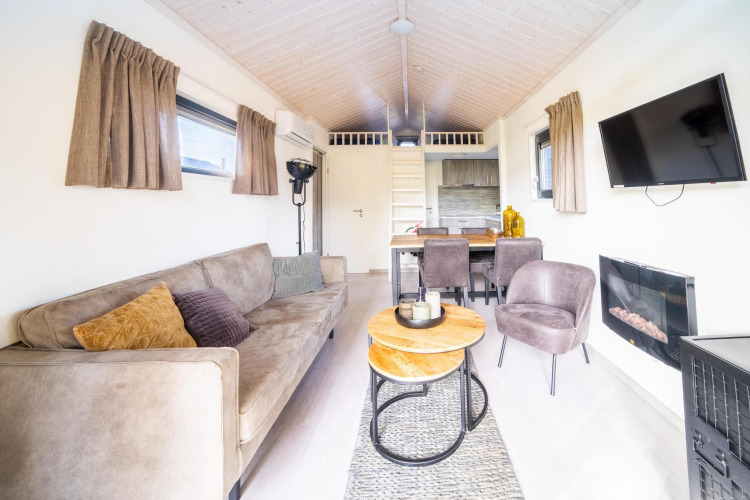 Bright and cozy living area in the Tiny House at De Wije Werelt, Netherlands, with sofa, table, and TV.