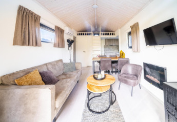 Lys og hyggelig stue i en tiny house-lodge på De Wije Werelt i Holland med sofa, spisebord og tv.