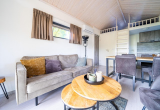 Sala moderna en el Tiny House de De Wije Werelt, Países Bajos, con sofá, comedor y entrepiso visible.