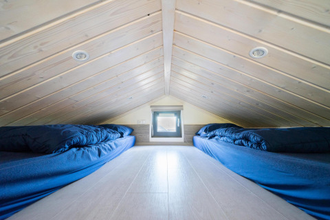 Slaapzolder in Tiny House bij De Wije Werelt, Nederland, met blauwe dekbedden op matrassen onder schuin dak.