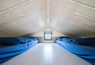 Chambre mezzanine dans Tiny House à De Wije Werelt, Pays-Bas, avec deux lits et linge bleu sous plafond incliné.