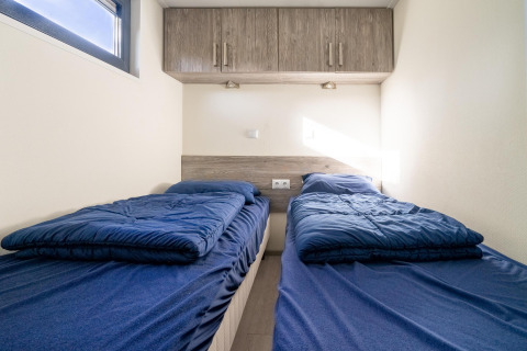 Zwei Einzelbetten mit blauer Bettwäsche in einem kompakten Zimmer im Tiny House bei De Wije Werelt, Niederlande.
