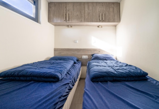 Dos camas individuales con sábanas azules en una pequeña habitación de Tiny House en De Wije Werelt, Países Bajos.