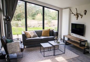 Modernes Wohnzimmer im Pavilion bei De Wije Werelt, Niederlande, mit großen Fenstern und stilvoller Einrichtung.