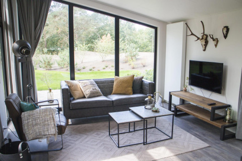 Modernes Wohnzimmer im Pavilion bei De Wije Werelt, Niederlande, mit großen Fenstern und stilvoller Einrichtung.