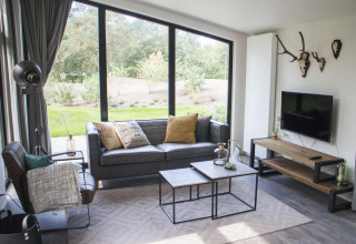 Modernes Wohnzimmer im Pavilion bei De Wije Werelt, Niederlande, mit großen Fenstern und stilvoller Einrichtung.
