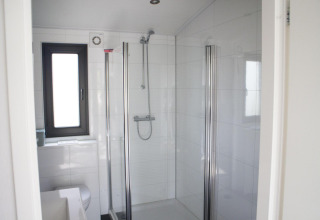 Baño moderno con ducha de vidrio, ventana y azulejos blancos en Pavilion en De Wije Werelt, Países Bajos.