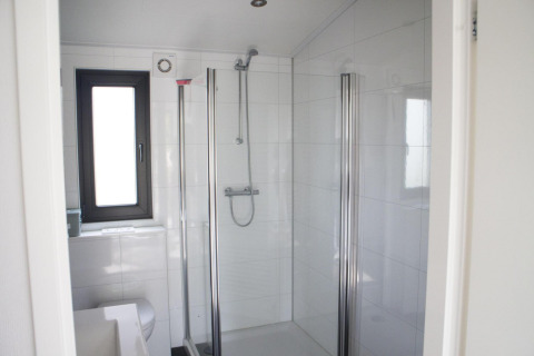 Baño moderno con ducha de vidrio, ventana y azulejos blancos en Pavilion en De Wije Werelt, Países Bajos.