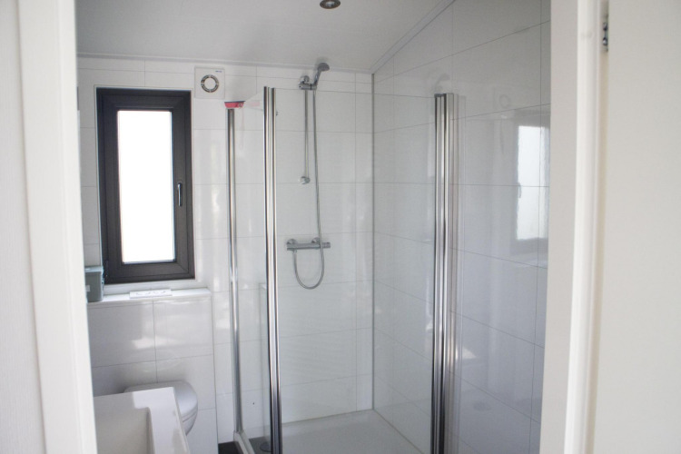 Baño moderno con ducha de vidrio, ventana y azulejos blancos en Pavilion en De Wije Werelt, Países Bajos.