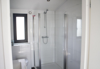 Moderne badkamer met glazen douche, raam en witte tegels in Pavilion op De Wije Werelt, Nederland.