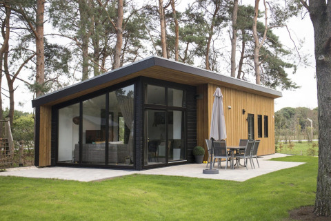 Lodge tipo pabellón moderno con grandes ventanales rodeado de árboles en De Wije Werelt, Países Bajos, exterior.