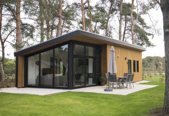Moderne pavillon-lodge med store glasvinduer omgivet af skov på De Wije Werelt, Holland, set udefra.