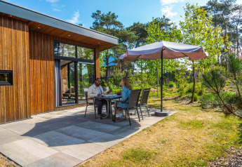 Two people dining outside Pavilion lodge at De Wije Werelt in the Netherlands, surrounded by nature.