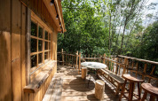 Terraza de casa en el árbol con muebles rústicos en Cosy Cabins, rodeada de bosque en Limburgo, Bélgica.