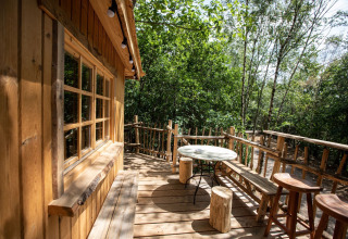 Terraza de casa en el árbol con muebles rústicos en Cosy Cabins, rodeada de bosque en Limburgo, Bélgica.
